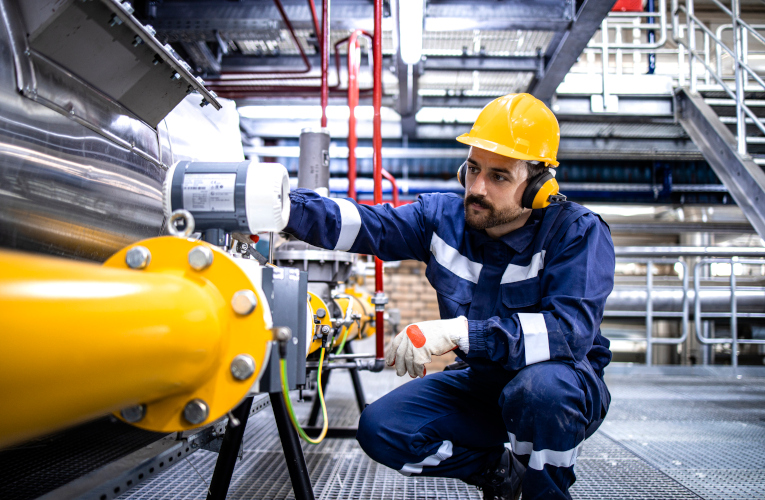 Refinery blue collar worker standing by LPG pipeline and checking gas production or distribution.